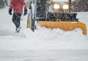 Person walking during heavy snowfall with tractor Plowing streets during snow storm winter