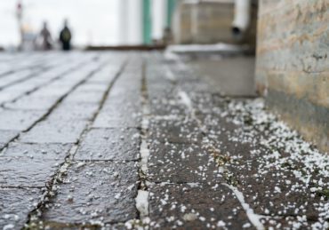 Closeup of technical salt grains on icy sidewalk surface in winter, used for melting ice and snow.