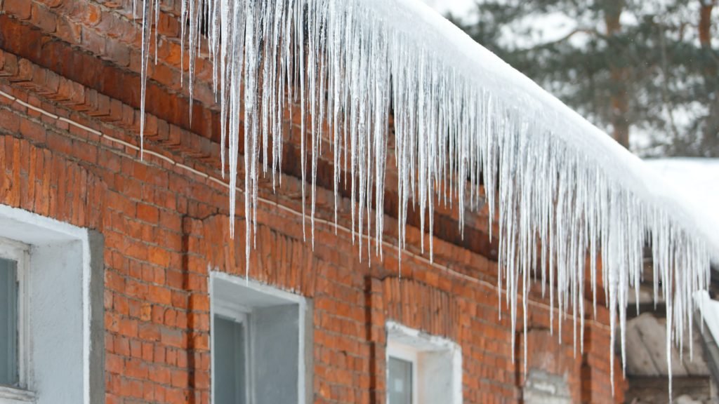 Ice stalactite hanging from the roof with red brick wall