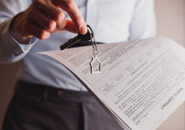 Manager offers keys to house holding contract in other hand. Rental and buying a property