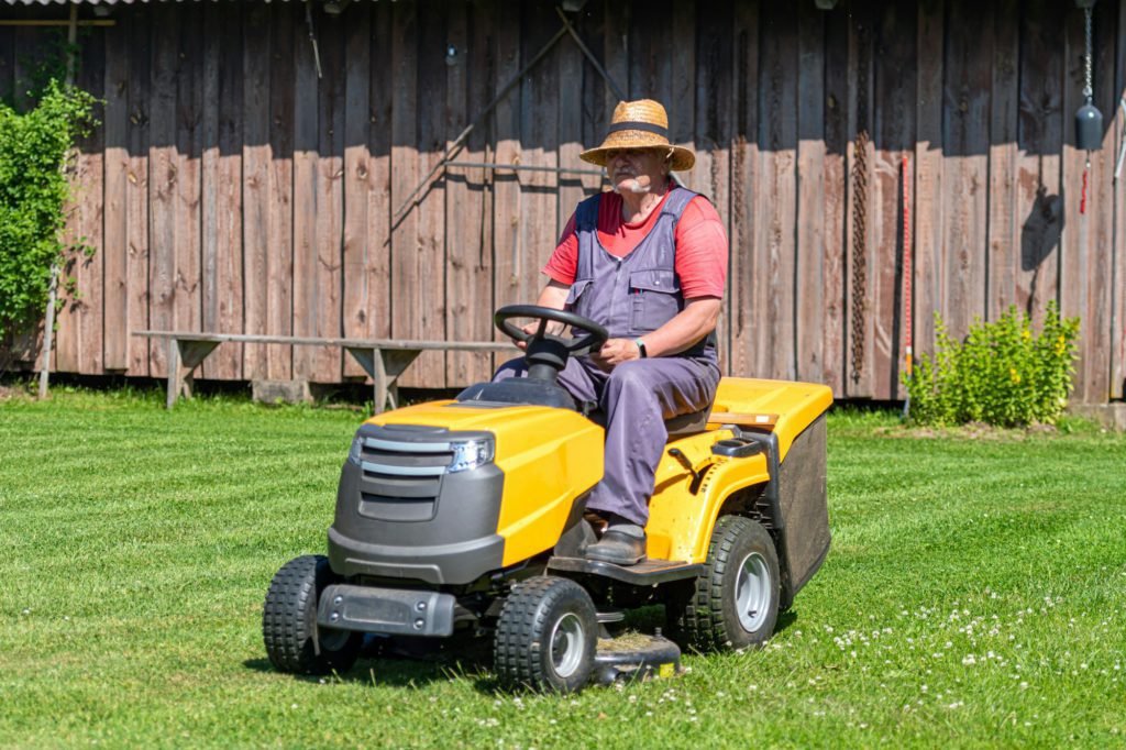 a senior man with a lawn mower mows the grass in the yard of country house