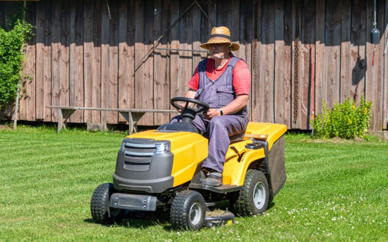 a senior man with a lawn mower mows the grass in the yard of country house