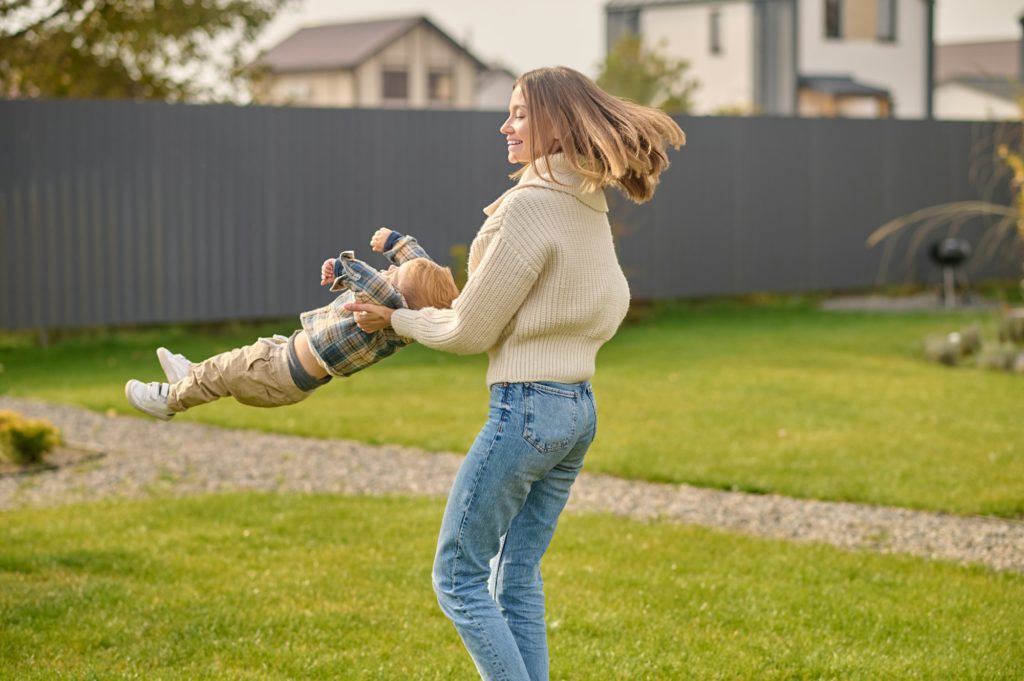 Joyful woman whirl child on lawn