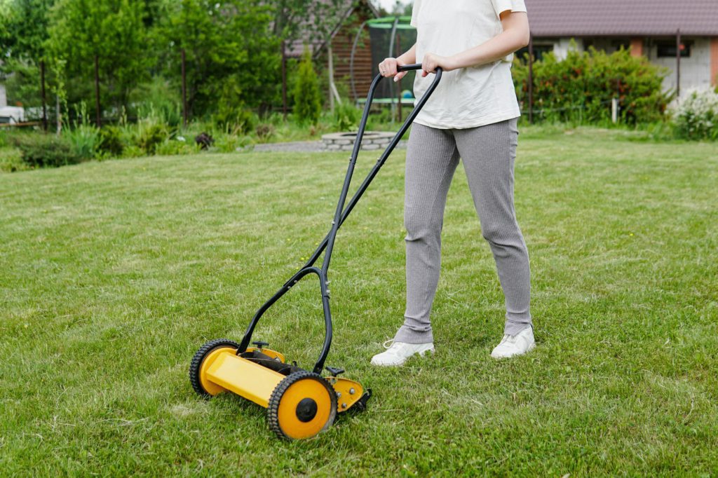 Young woman mowing lawn with a manual push lawn mower