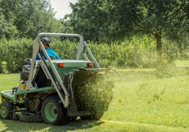 Professional gardener cutting green grass on lawn mower machine in park