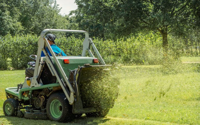 Professional gardener cutting green grass on lawn mower machine in park